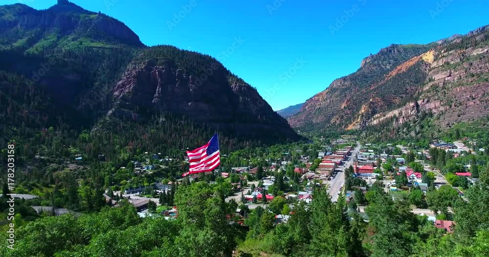 American Flag Waving In The Breeze Above Colorado Town In Mountain Valley Surrounded By Green Pines - Ouray, Colorado, USA