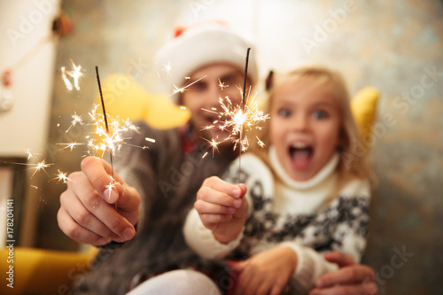 Close-up photo of overjoyed father in Santa's hat and his pretty daughter holding sparklers, selective focus on sparklers © Drobot Dean