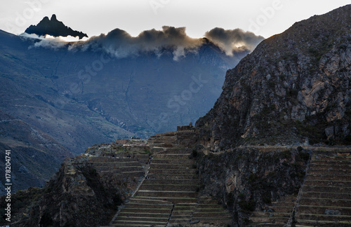 People walking on the terraces of Pumatallis, ancient Inca fortress and mountains covered in clouds, Sacred Valley, Ollantaytambo, Peru