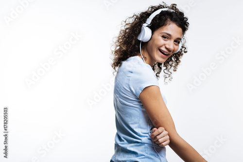 Lovely curly-haired woman listening to music and laughing