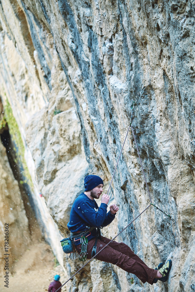 male rock climber climbs on a rocky wall at winter sunny day. Man climber in warm clothes on yellow cliff.