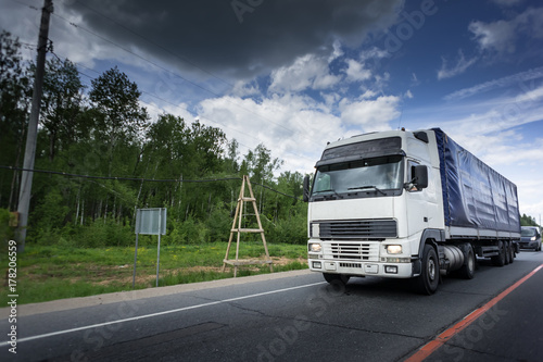 White truck driving on asphalt road in a rural landscape. dark clouds and blue sky