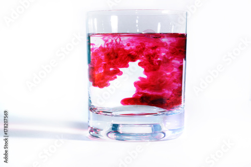 On a white background transparent glasses with water, in each drip red paint. Ink blurs in the water, form beautiful patterns.