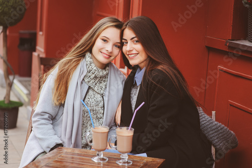 two happy girl friends talking and drinking coffee in autumn city in cafe. Meeting of good friends  young fashionable students with natural make up.