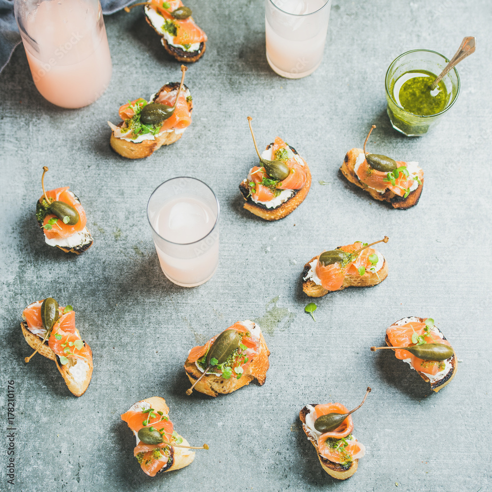 Φωτογραφία Crostini with smoked salmon, pesto sauce, watercress and capers and pink grapefruit cocktails over grey background, top view, square crop