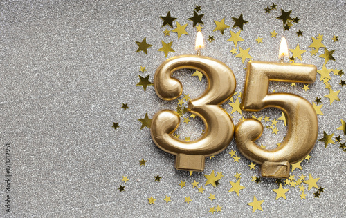 Number 35 gold celebration candle on star and glitter background