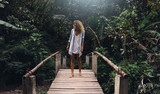 A travel blogger female is exploring wild jungles in exotic country. A tourist woman is visiting national park of tropical plants. Young woman with curly hair is impressed with beautiful wild nature.