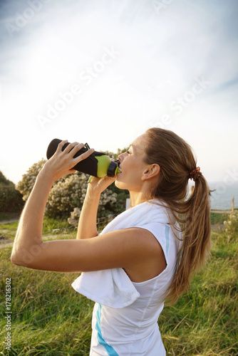 Portrait of fitness girl drinking water from bottle on jogging session