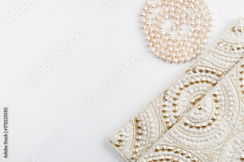 Female white bag and pearl necklace on a white background top view