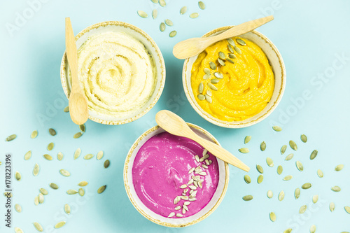 bright appetizers in the form of sauces on a blue background among pumpkin seeds. Hummus, carrot and beetroot sauces. Top view. Flat lay © svitlini