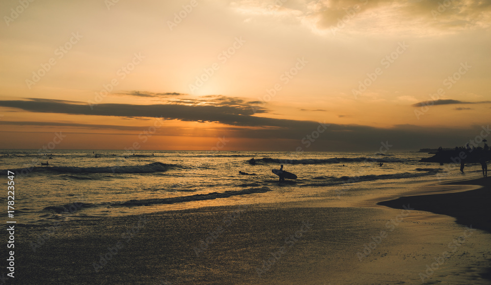 Outstanding sea view at the nightfall with silhouettes of surfers. Colorful dawn at the tropical sand beach. Young surfers are spending summer vacation riding waves at the tropical country. Outstanding sea view at the nightfall with silhouettes of surfers. Colorful dawn at the tropical sand beach. Young surfers are spending summer vacation riding waves at the tropical country.
