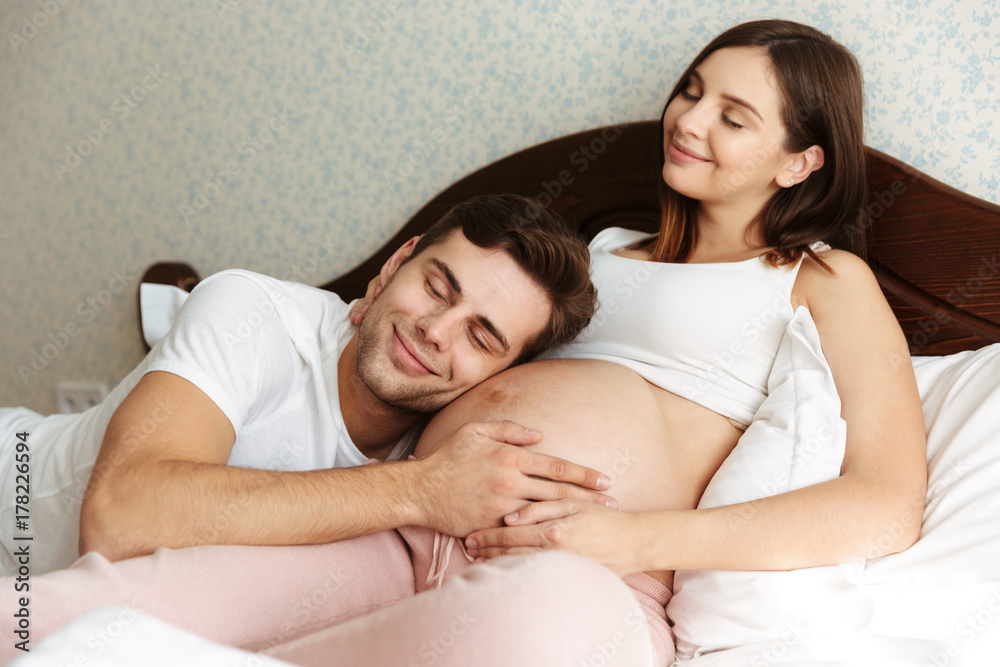 Delighted young pregnant wife lying in bed Delighted young pregnant wife lying in bed
