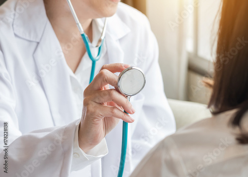 Healthcare concept with cardiologist doctor examining woman patient's heart health diagnosing cardiovascular disease illness symptom using stethoscope in medical clinic or hospital service center photo