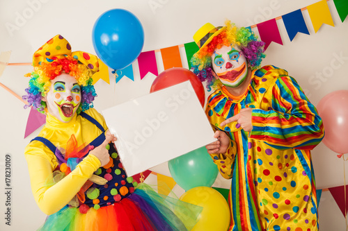 Two clowns boy and girl on holiday with white plate in hands. Birthday of the child.