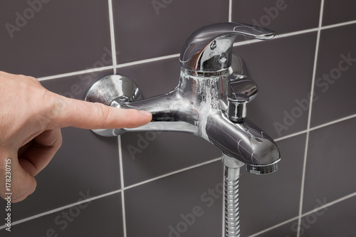 Man's hand finger pointing to calcified water tap in the bathroom. Problem concept. photo