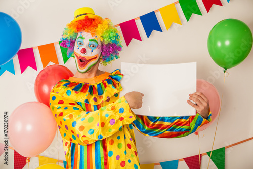 A cheerful, bright clown with a white signboard for the inscriptions in his hands. Birthday of the child.