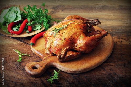 Whole roasted chicken on cutting board. Wooden rustic background