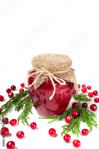 Jam from berries of cranberries in a glass jar close-up with copy space on white background with spruce branches and cones isolate