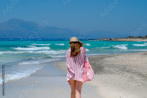 Young girl in a straw hat on the beach enjoying the beautiful view. View from the back.