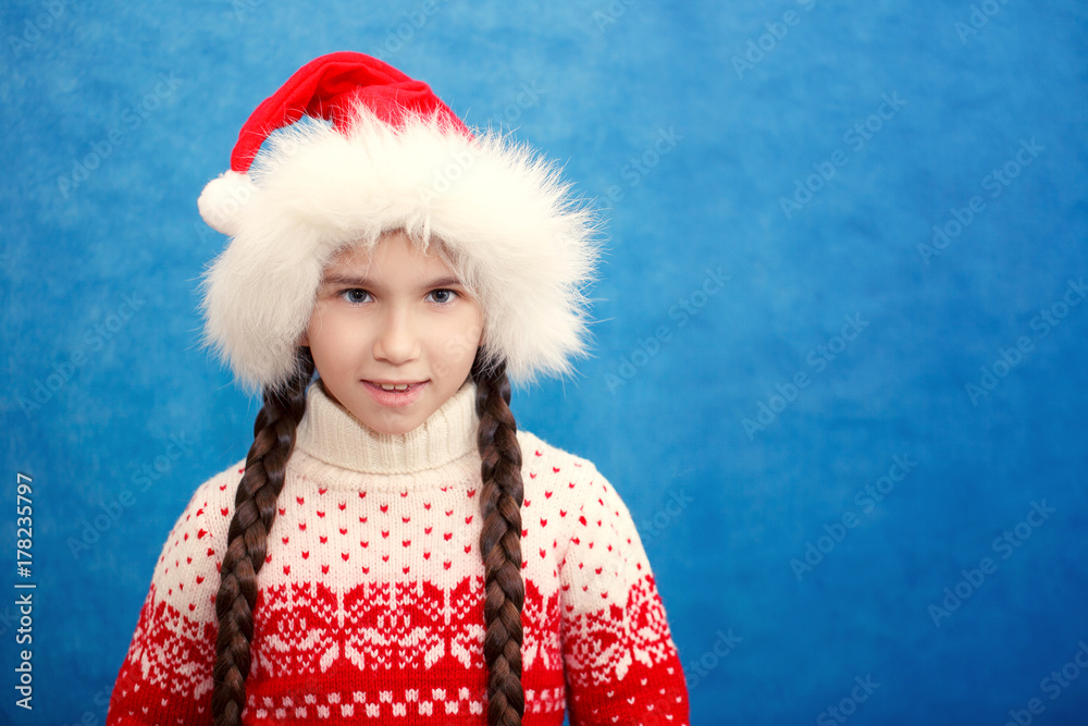 Cute smiling little girl in Santa hat and red sweater on blue background close-up. Cute smiling little girl in Santa hat and red sweater on blue background close-up.
