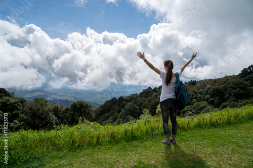 Portrait of beautiful Asian woman trekking on top of a hill looking at the environment. Trekking, nature, clean environment concept. Holding hands up in the air. Copy space.