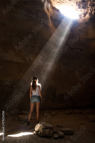 Beautiful young girl seeing the light, having spiritual experience in sunbeam while alone in a cave