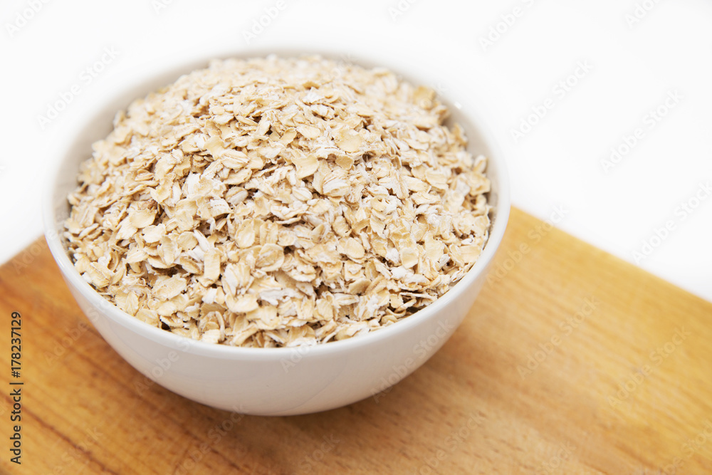 oat flakes in a white bowl on cutting board on a white background oat flakes in a white bowl on cutting board on a white background