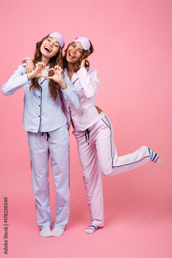 Pretty two girls friends in pajamas showing heart love gesture. Pretty two girls friends in pajamas showing heart love gesture.