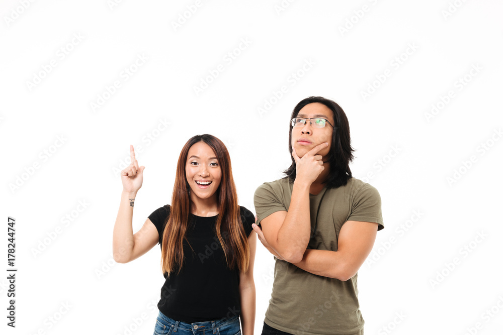 Portrait of a thoughtful smiling asian couple pointing finger up Portrait of a thoughtful smiling asian couple pointing finger up