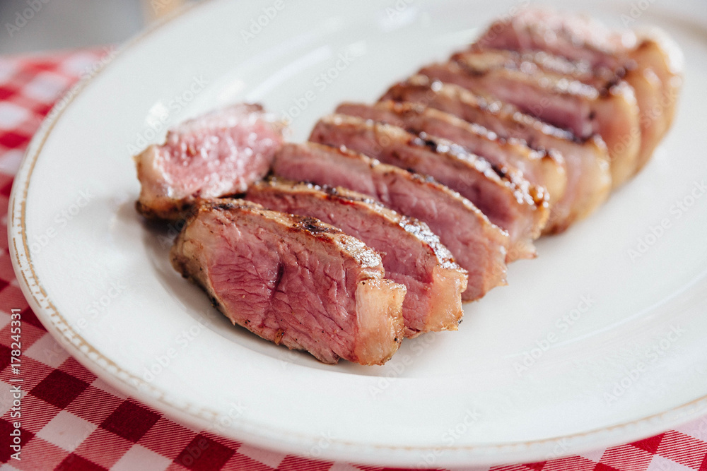 Close up Sliced medium rare charcoal grilled boneless wagyu Top Loin steak in white plate on red and white pattern tablecloth.