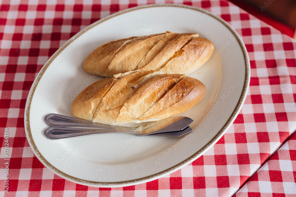 Fresh baked bread for eating with steak in white plate on red and white pattern tablecloth. Fresh baked bread for eating with steak in white plate on red and white pattern tablecloth.