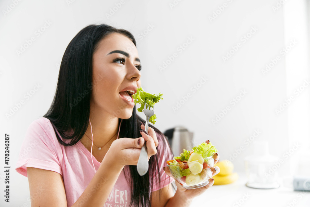 Smiling woman eats salad in the white kitchen Smiling woman eats salad in the white kitchen
