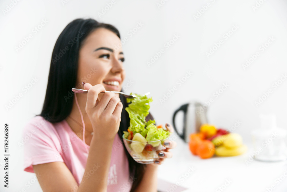 Smiling woman eats salad in the white kitchen Smiling woman eats salad in the white kitchen