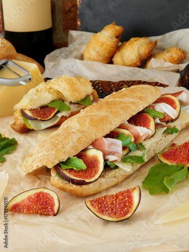 Sandwich with hamon, figs, arugula and Parmesan cheese. Baked products, a bottle of wine and ingredients in the background