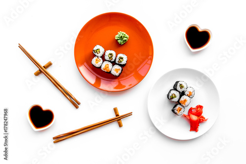 Sushi roll with salmon and avocado on plate with soy sauce, chopstick, wasabi on white background top view