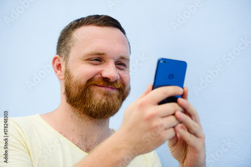 cheerful man with a red beard looks into the phone on a blue background