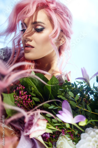 Fototapeta Naklejka Na Ścianę i Meble -  Beautiful woman with pink hair holds large bouquet with greenery and violet flowers