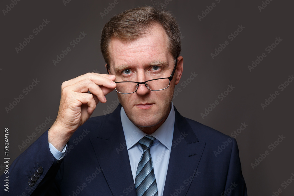 Adult man in a business suit strictly looks over his glasses Adult man in a business suit strictly looks over his glasses