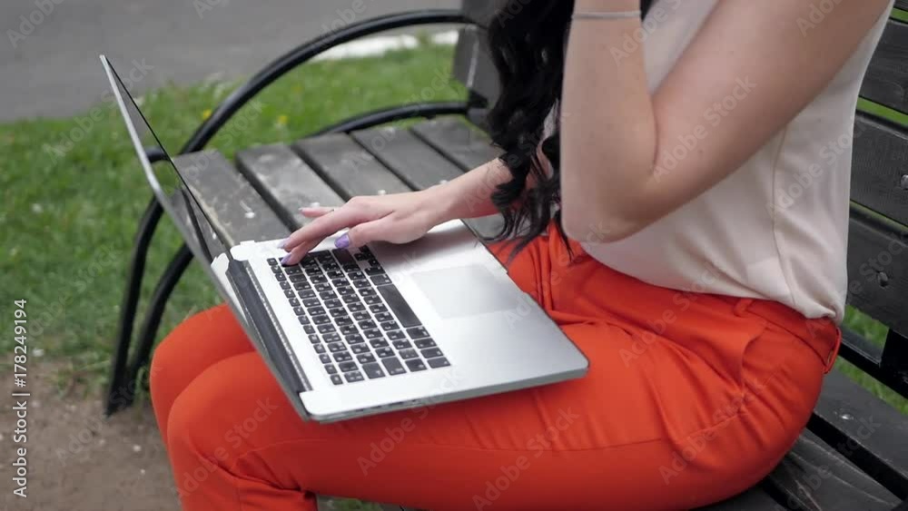 Beautiful woman sits on a park bench with a laptop typing on the keyboard