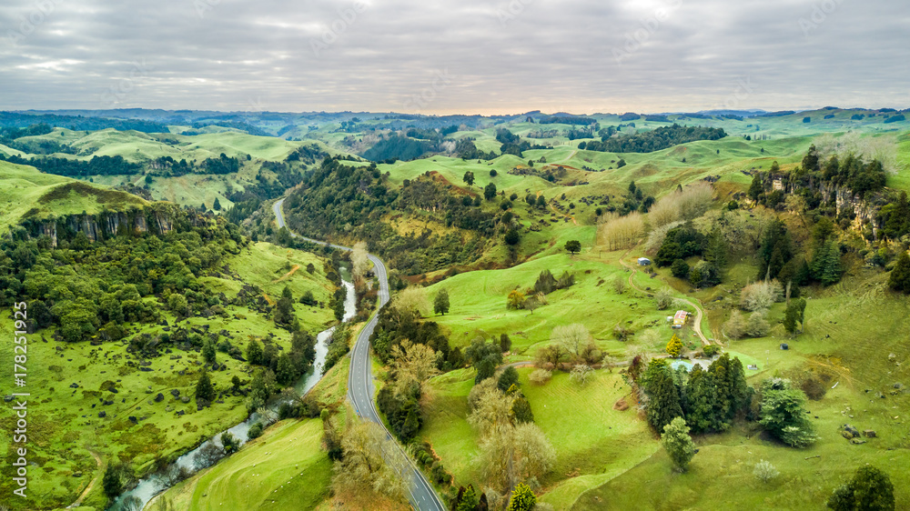 Obraz premium Aerial view on a road running along a river through mountain valley with rocks on the background. Taranaki region, New Zealand