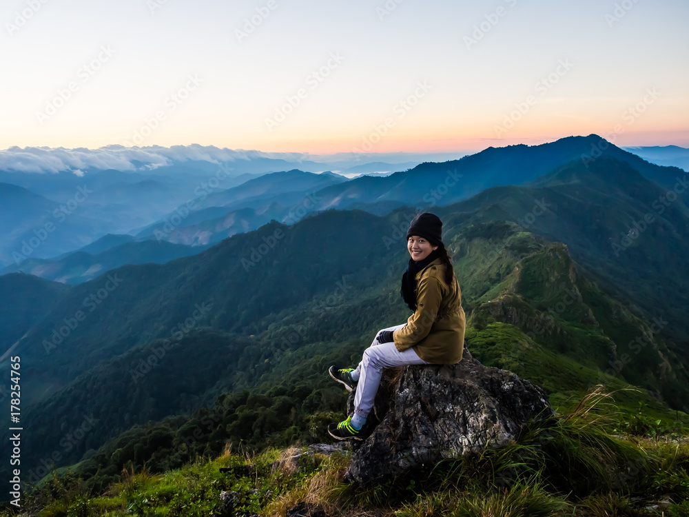 A woman turns back with a happy smile on her face for her portrait photo with the great view of mountain ridge with beautiful cloudy sky in the morning. This great nature landscape is at Doi Phu Wae
