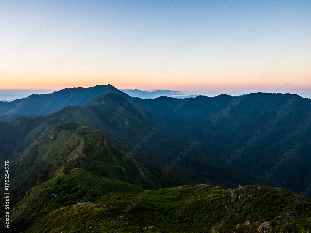 The valley of two ranges of mountain ridge at Doi Phu Wae in Nan, Thailand. The place is surround by green nature with the morning sunrise sky behind
