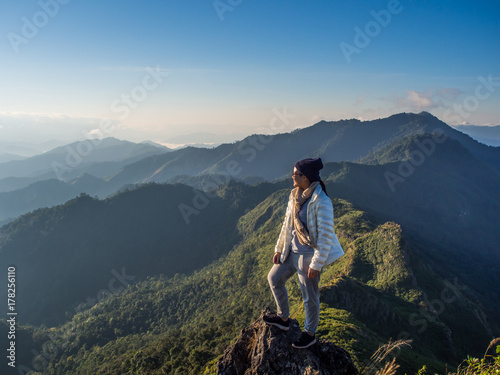 A happy girl is posting a cool act and looking toward a white morning sunlight. This is a great view point of her with the surrounding of the green nature from a great mountain ridge range in Thailand