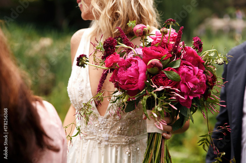 Obraz na plátně Pretty bride holds rich dark pink bouquet of peonies in her arm