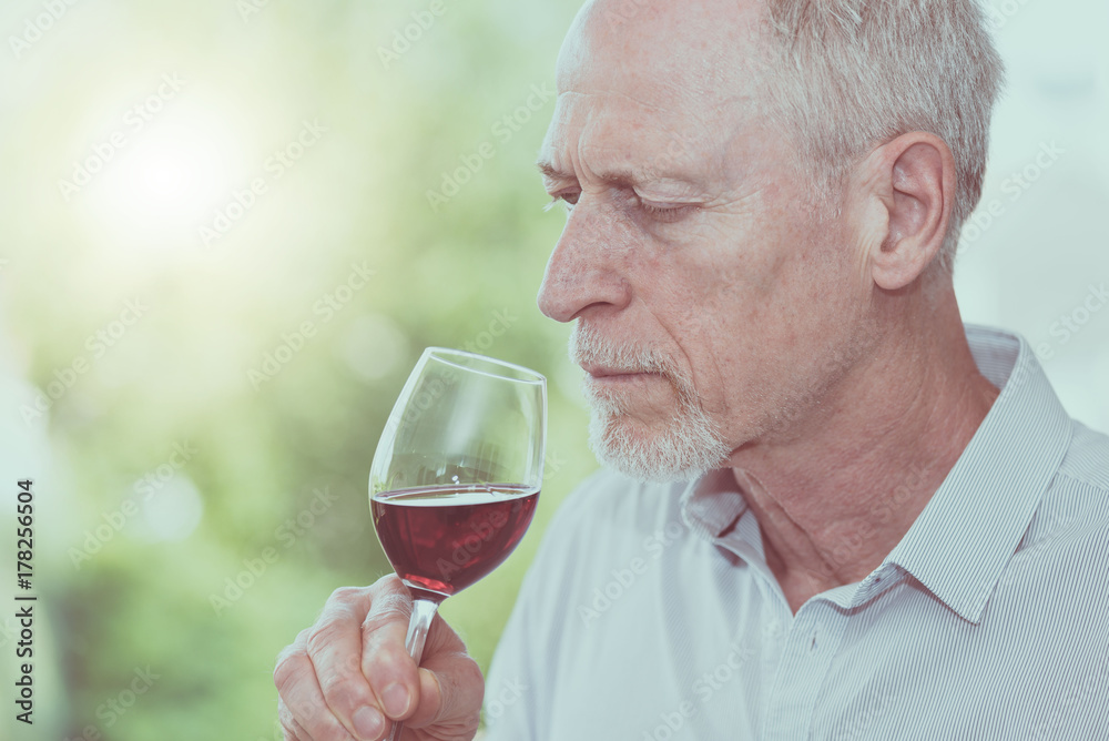 Mature man tasting red wine, light effect