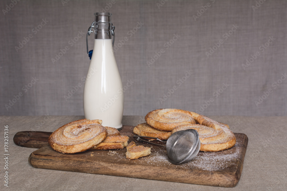 Milk bottle and sweet cookies with powdered sugar on a wooden board Milk bottle and sweet cookies with powdered sugar on a wooden board