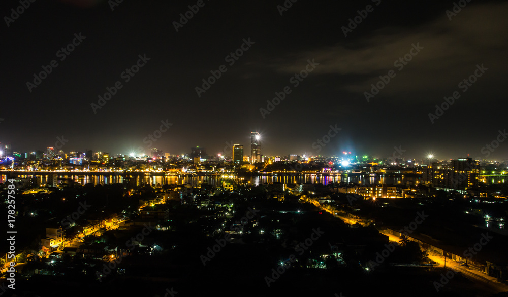 Fototapeta premium Night cityscape photo of Phnom Penh, the capital city of Cambodia. The yellow street light grow perspectively in both side leading to a long way reflection light at the river