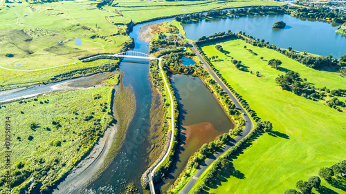 Aerial view on a beautiful bridge across a small stream with residential suburb on the background. New Zealand