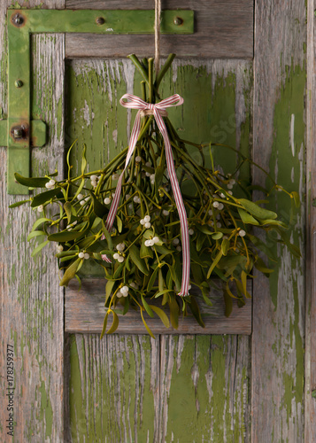 Canvas Print Christmas mistletoe with white and red ribbon bow hanging on a rustic green wooden door
