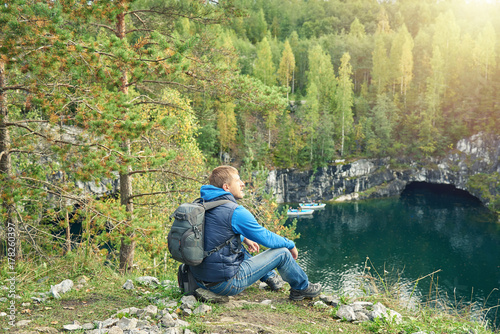 Man with backpack sitting on the ground and looking at the beautiful lake at a canyon.